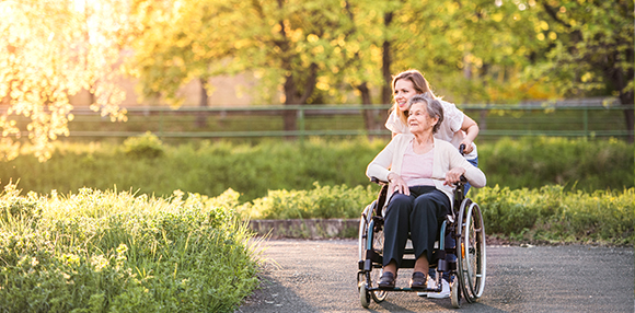 an elderly lady in a wheel chair being wheeled around by a woman through a park