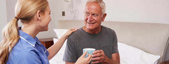 a nurse handing a mug to an elderly man sitting on a bed